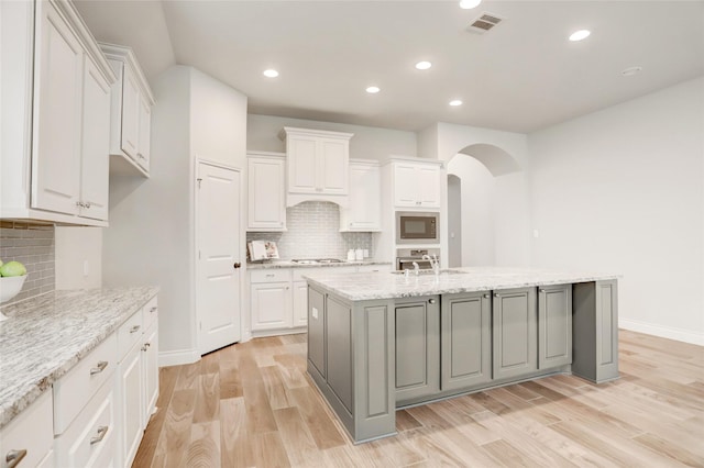 kitchen featuring stainless steel appliances, arched walkways, white cabinets, and light wood-style floors