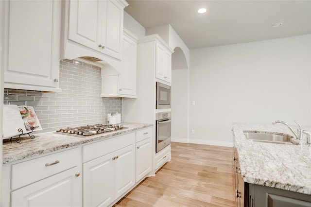 kitchen featuring white cabinets, light wood-style flooring, appliances with stainless steel finishes, a sink, and backsplash