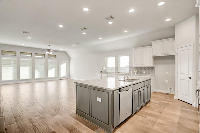 kitchen featuring light wood finished floors, a center island with sink, stainless steel dishwasher, white cabinetry, and a sink