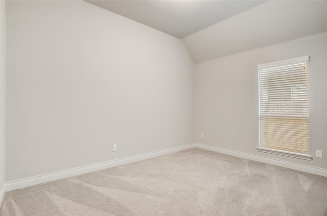 unfurnished room with light colored carpet, vaulted ceiling, and baseboards
