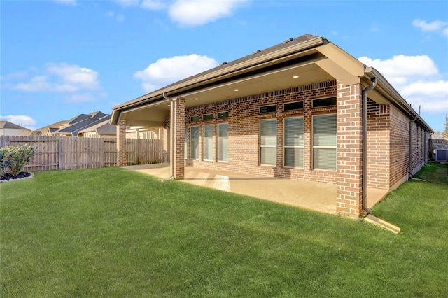 rear view of house with brick siding, a patio, a lawn, central AC, and fence