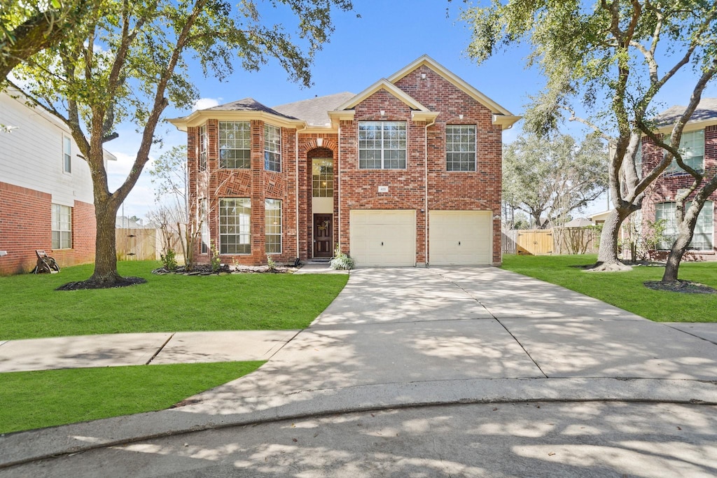 traditional-style home featuring driveway, brick siding, an attached garage, fence, and a front yard