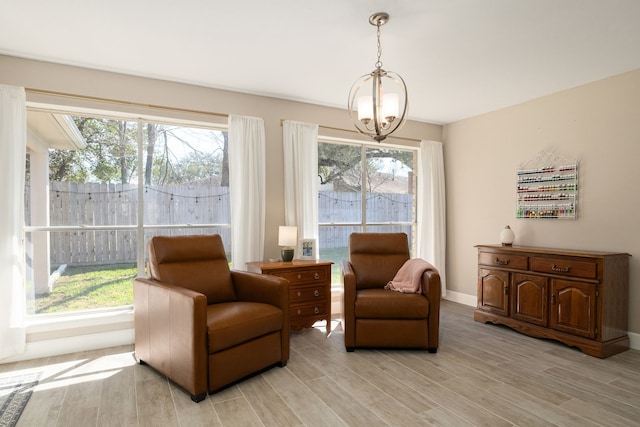 living area with a notable chandelier, baseboards, a wealth of natural light, and light wood-style floors