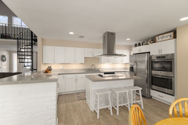 kitchen featuring a sink, white cabinetry, a kitchen breakfast bar, appliances with stainless steel finishes, and island exhaust hood