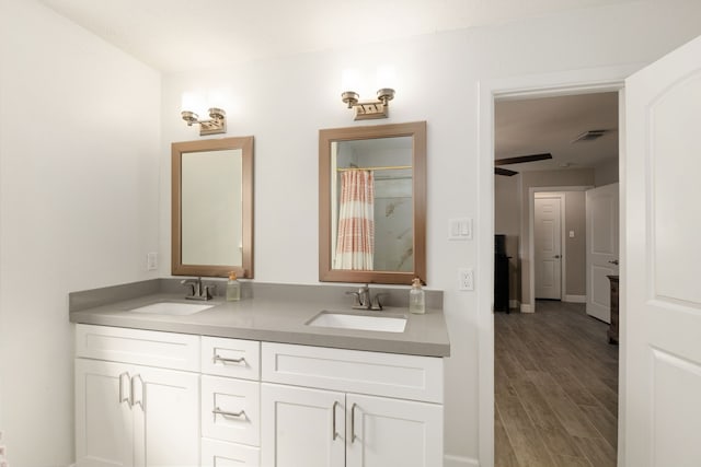 full bath with double vanity, a shower with shower curtain, a sink, and wood finished floors