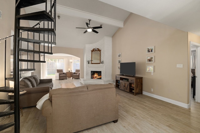 living room with a brick fireplace, baseboards, arched walkways, light wood-style floors, and beam ceiling