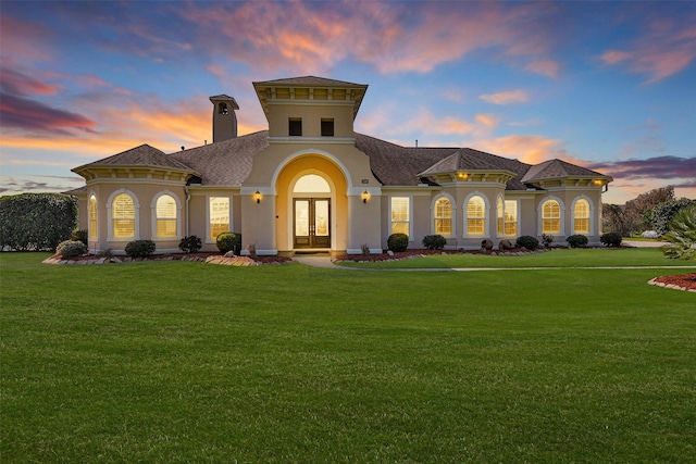 mediterranean / spanish-style home with stucco siding, french doors, a yard, roof with shingles, and a chimney