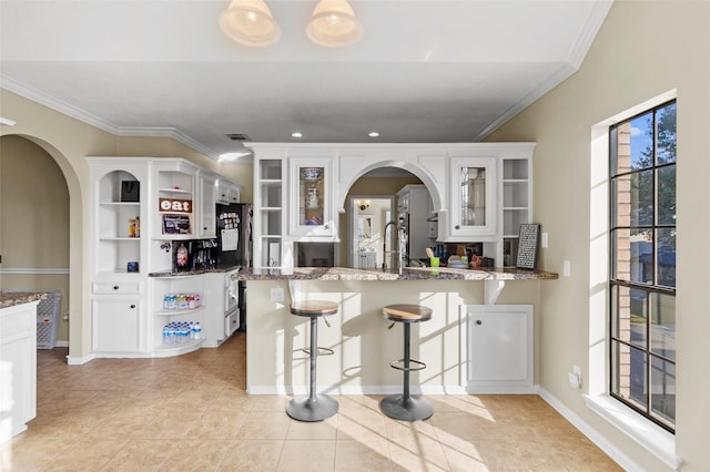 kitchen featuring stone counters, arched walkways, white cabinetry, and open shelves