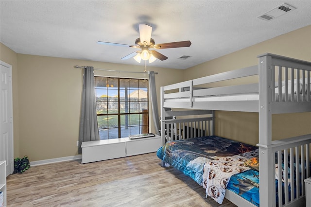 bedroom with a ceiling fan, a textured ceiling, visible vents, and wood finished floors