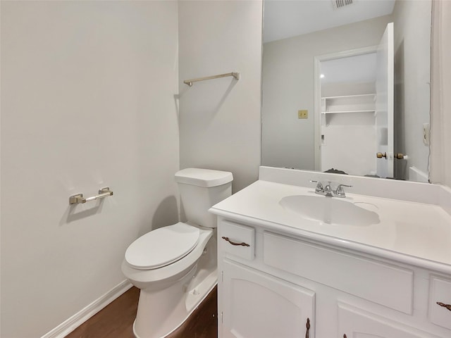 half bathroom with visible vents, baseboards, toilet, wood finished floors, and vanity