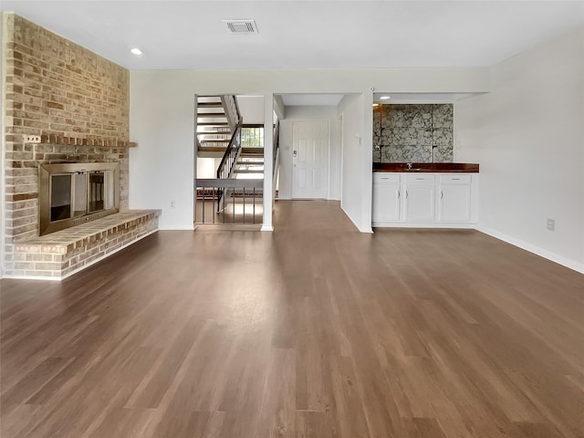 unfurnished living room with a brick fireplace, baseboards, visible vents, and wood finished floors