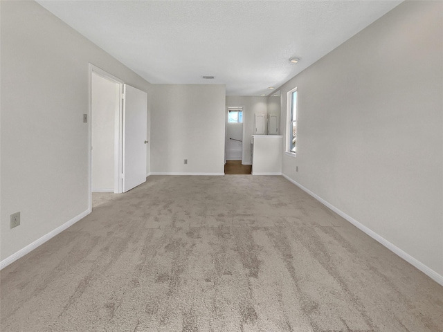 spare room with a textured ceiling, carpet, visible vents, and baseboards