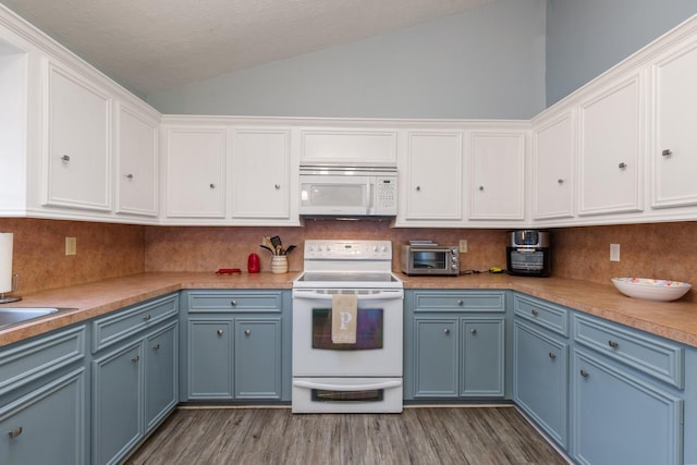 kitchen featuring white appliances, white cabinets, vaulted ceiling, blue cabinetry, and backsplash