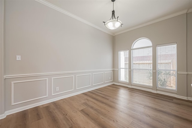 spare room featuring a wainscoted wall, crown molding, a decorative wall, and wood finished floors