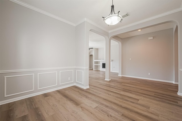 spare room featuring arched walkways, a fireplace, visible vents, ornamental molding, and wood finished floors