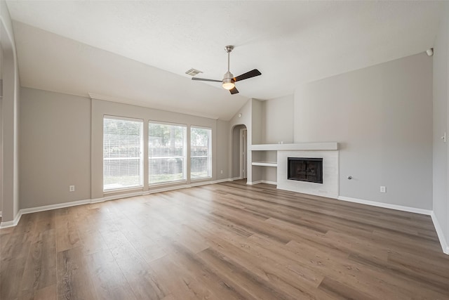 unfurnished living room featuring lofted ceiling, visible vents, a tiled fireplace, a ceiling fan, and wood finished floors