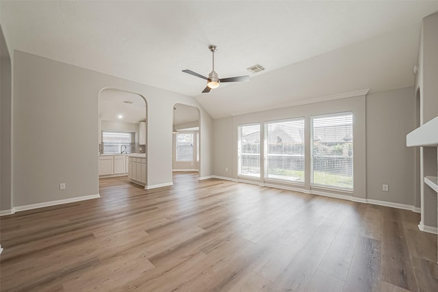 unfurnished living room with arched walkways, lofted ceiling, visible vents, ceiling fan, and light wood-type flooring