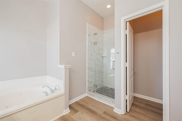 bathroom featuring a stall shower, baseboards, a bath, and wood finished floors