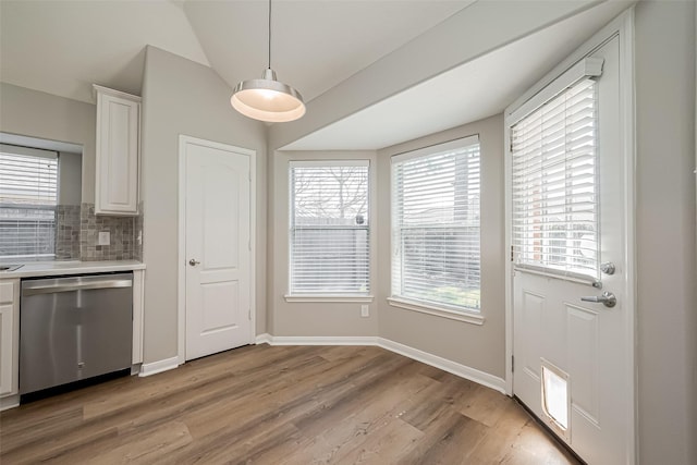 kitchen featuring lofted ceiling, light wood-style flooring, stainless steel dishwasher, white cabinetry, and backsplash