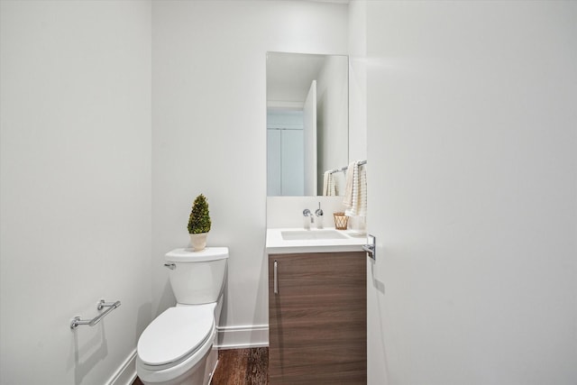 half bath with toilet, baseboards, wood finished floors, and vanity