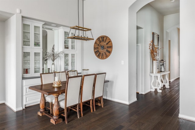 dining area featuring arched walkways, dark wood-style flooring, and baseboards