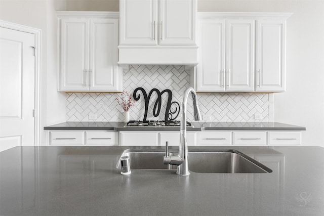 kitchen featuring dark countertops, tasteful backsplash, white cabinetry, and a sink