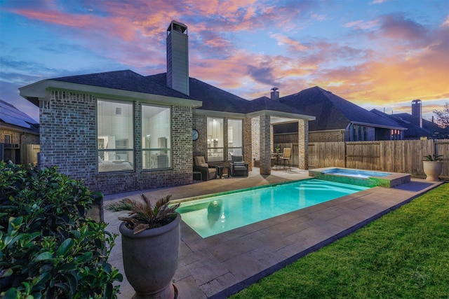 pool at dusk featuring a patio area, a fenced backyard, and a pool with connected hot tub