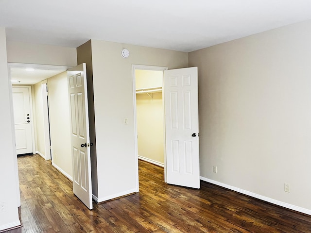 unfurnished bedroom with a walk in closet, baseboards, dark wood-style flooring, and a closet