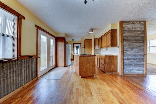 kitchen featuring light wood-type flooring, freestanding refrigerator, brown cabinetry, and a textured ceiling