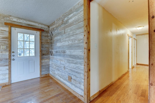 interior space featuring a textured ceiling, wood walls, baseboards, and light wood-style floors