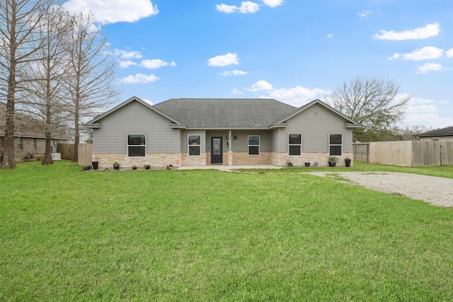 rear view of house featuring fence, a yard, stone siding, roof with shingles, and driveway