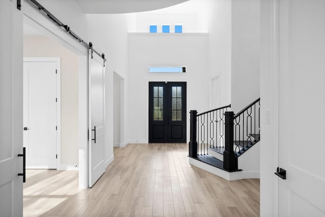 entrance foyer with a barn door, baseboards, a towering ceiling, stairs, and light wood-style floors