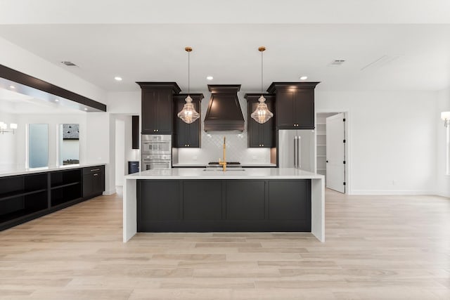 kitchen featuring custom exhaust hood, light wood finished floors, stainless steel appliances, light countertops, and backsplash