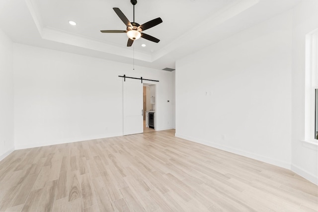 unfurnished room with ceiling fan, a barn door, recessed lighting, light wood-type flooring, and a raised ceiling