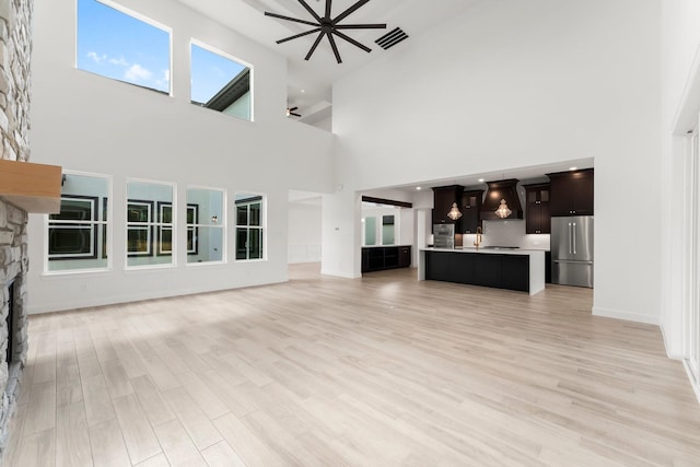 unfurnished living room featuring visible vents, ceiling fan, a fireplace, and light wood-style flooring