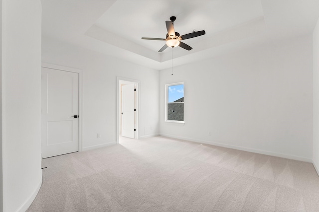 spare room with carpet floors, a tray ceiling, a ceiling fan, and baseboards