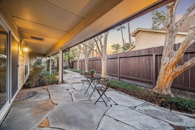 patio terrace at dusk with a fenced backyard and visible vents