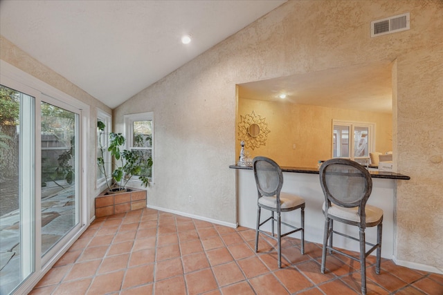 kitchen featuring a textured wall, tile patterned flooring, visible vents, and vaulted ceiling