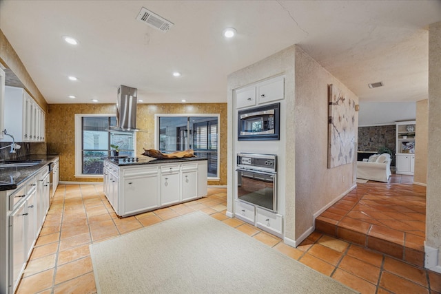 kitchen featuring visible vents, white cabinets, a sink, island range hood, and black appliances