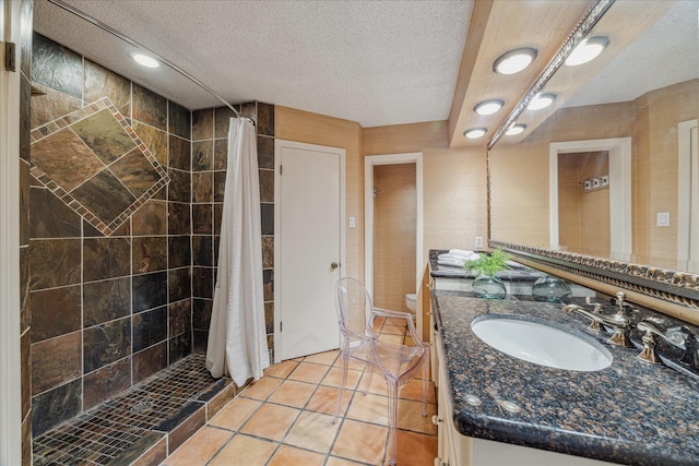 bathroom with toilet, a textured ceiling, a tile shower, and vanity