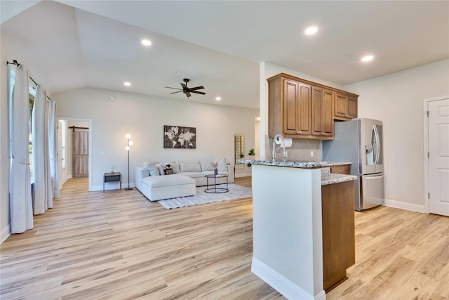 kitchen with light stone counters, brown cabinets, light wood-style flooring, open floor plan, and stainless steel fridge