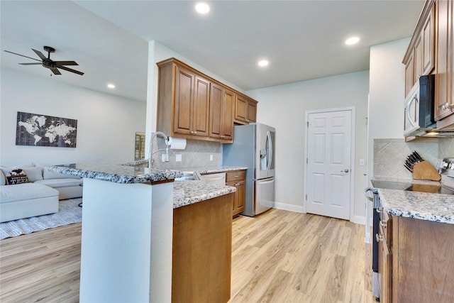 kitchen featuring open floor plan, stainless steel appliances, light wood-type flooring, and a peninsula