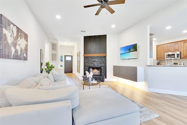 living area featuring recessed lighting, visible vents, light wood-style floors, a stone fireplace, and baseboards