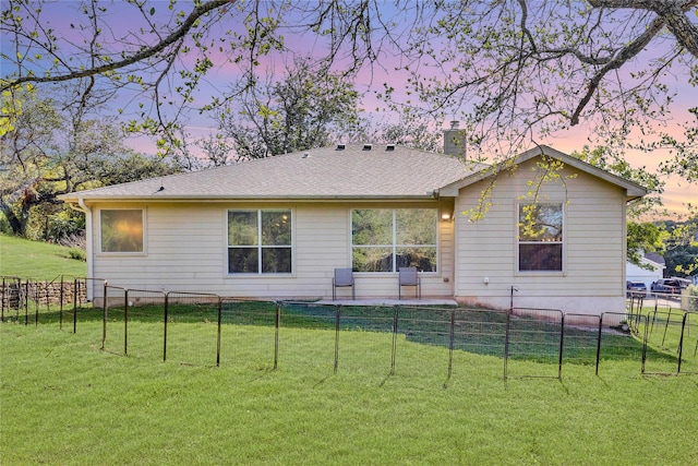 rear view of house with a shingled roof, a fenced backyard, a lawn, and a chimney