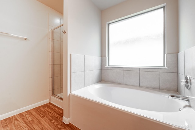 bathroom with a stall shower, baseboards, a garden tub, and wood finished floors