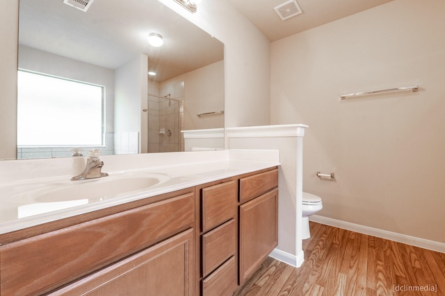 full bath with visible vents, toilet, wood finished floors, a tile shower, and vanity