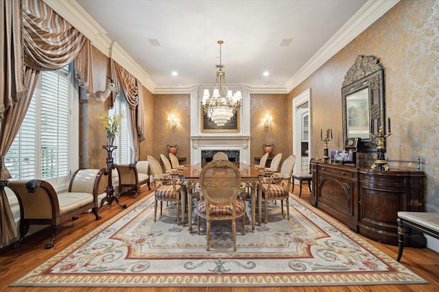 dining area featuring wallpapered walls, wood finished floors, crown molding, a fireplace, and a notable chandelier