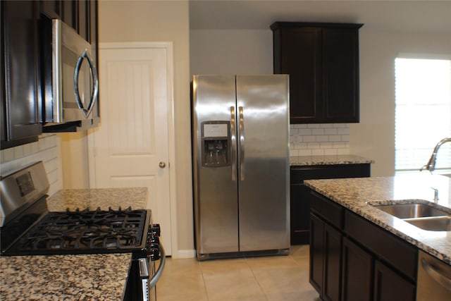 kitchen with light tile patterned floors, stainless steel appliances, decorative backsplash, a sink, and light stone countertops