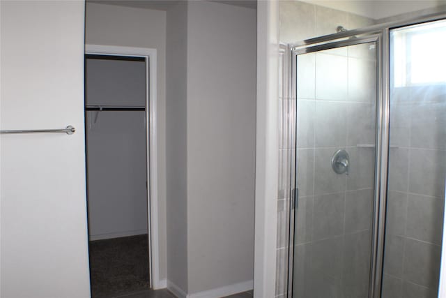 bathroom featuring a spacious closet, a shower stall, and baseboards