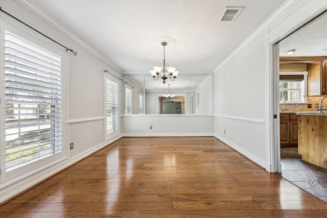 unfurnished dining area with a notable chandelier, visible vents, wood-type flooring, and ornamental molding